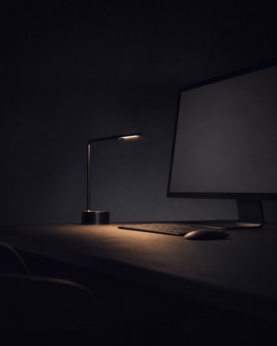 Mesa de trabalho à noite com luminária acesa e monitor
