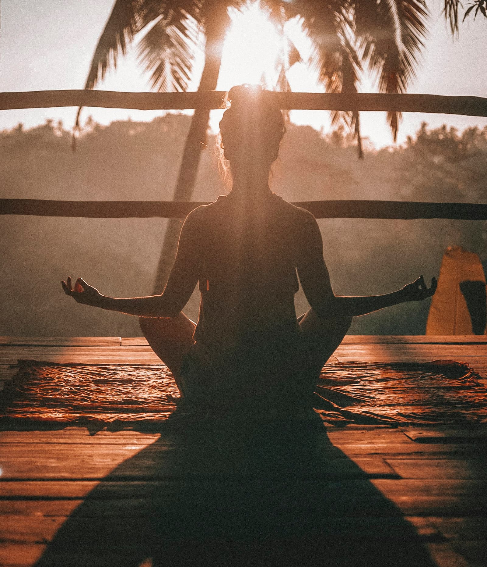 A person meditating cross-legged on a rock beside still water, surrounded by misty forested mountains at dawn